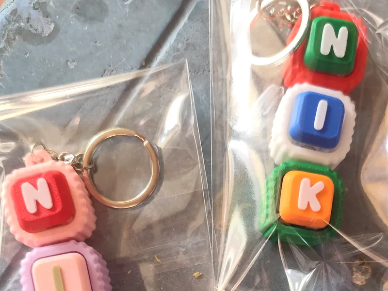 Keychain nama NIK dengan huruf pada butang berwarna-warni, dibungkus plastik